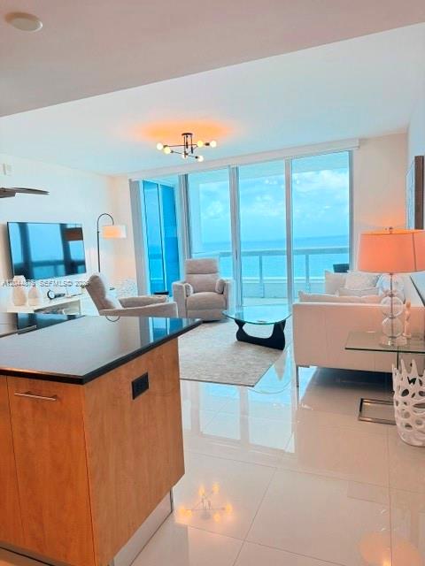 A modern living room features a kitchen island, light tile floors, and floor-to-ceiling ocean views — 6899 Collins Ave # 2201, Miami Beach FL 33141, MIAMI BEACH, FL