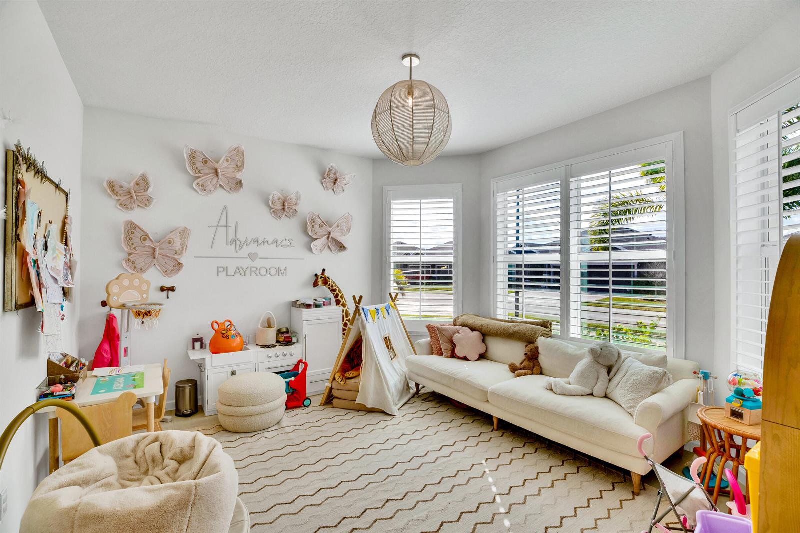 A bright playroom features a white sofa, a play tent, butterfly wall decor, and plantation shutters — VERO BEACH, FL
