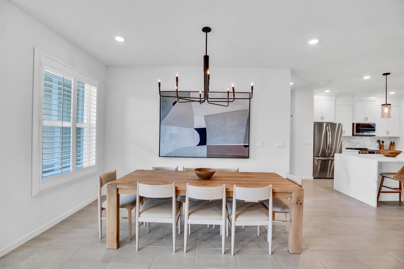 A dining room features a wooden table, six chairs, a modern chandelier, and abstract art — VERO BEACH, FL