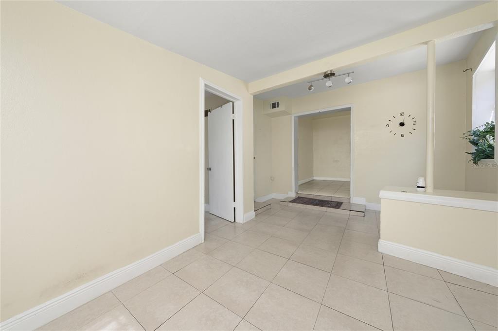 A room with light-colored tile flooring, cream walls, a wall clock, and a doorway — 4604 ROBBINS AVENUE, ORLANDO, FL