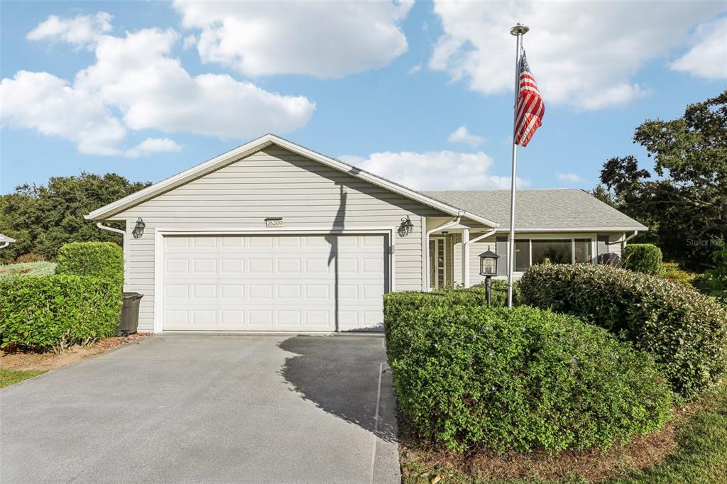 A single-story house with light gray siding, a two-car garage, and an American flag — 26209 NEWCOMBE CIRCLE, LEESBURG, FL