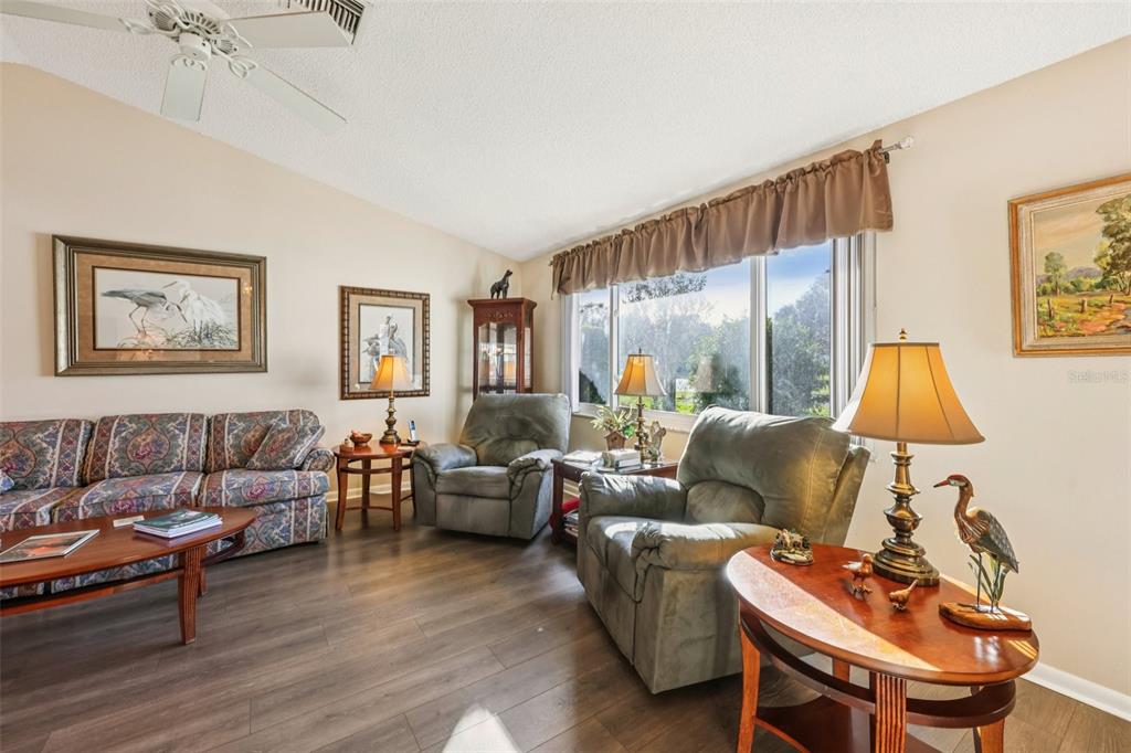 A living room features wood-look flooring, a patterned sofa, two recliners, and a large window — 26209 NEWCOMBE CIRCLE, LEESBURG, FL