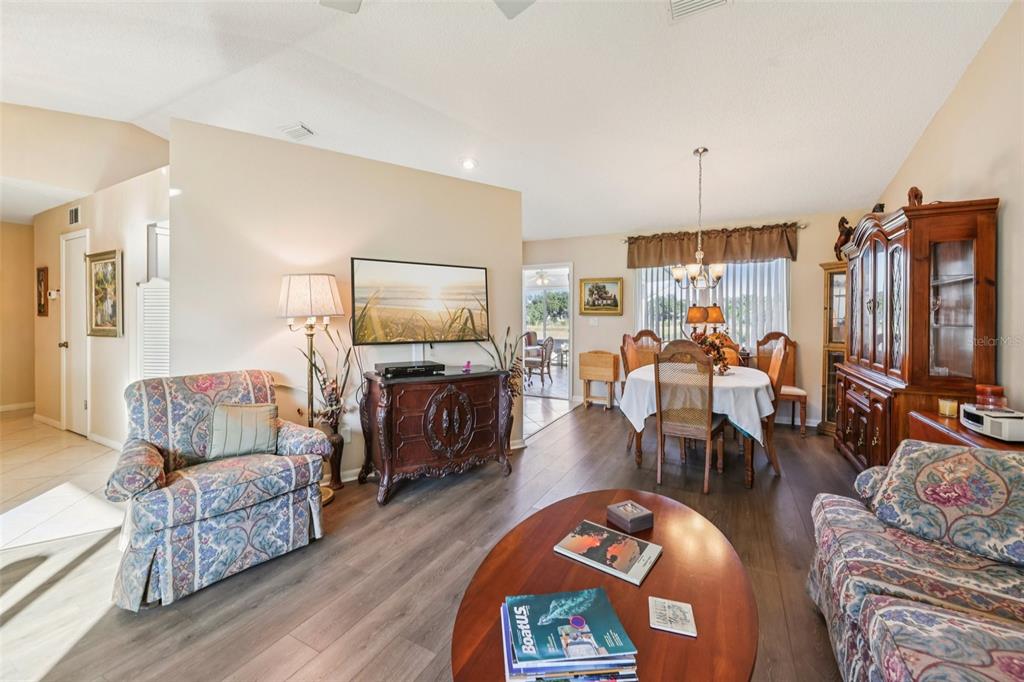 A living and dining area with wood-look flooring, floral furniture, and a large wooden hutch — 26209 NEWCOMBE CIRCLE, LEESBURG, FL