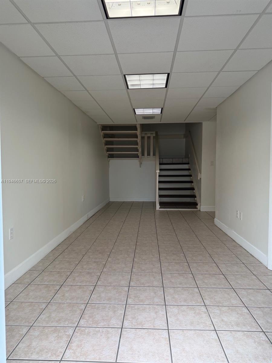An empty room features beige tiled floors, white walls, and a staircase leading upward — 16155 SW 117th Ave # B2, Miami FL 33177, MIAMI, FL