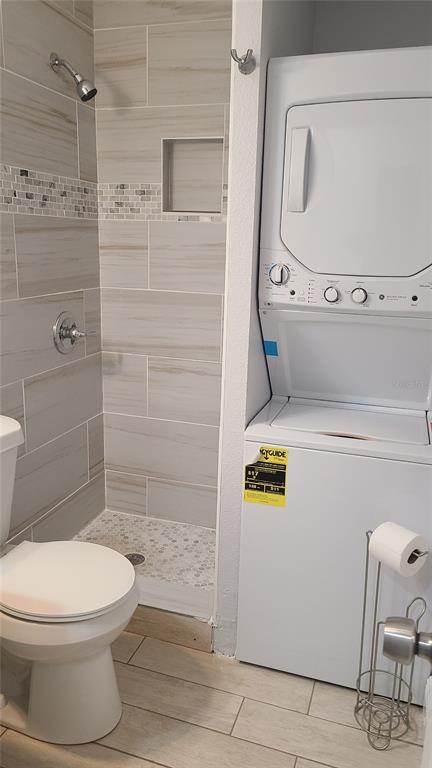 A bathroom featuring a tiled shower, a toilet, and a stacked washer and dryer unit — 1421 E 108TH AVENUE UNIT A, TAMPA, FL