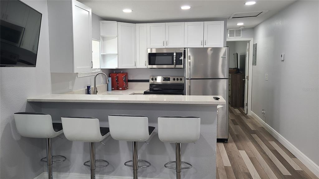 A kitchen features white cabinetry, stainless steel appliances, a breakfast bar with four stools, and flooring — 1421 E 108TH AVENUE UNIT A, TAMPA, FL