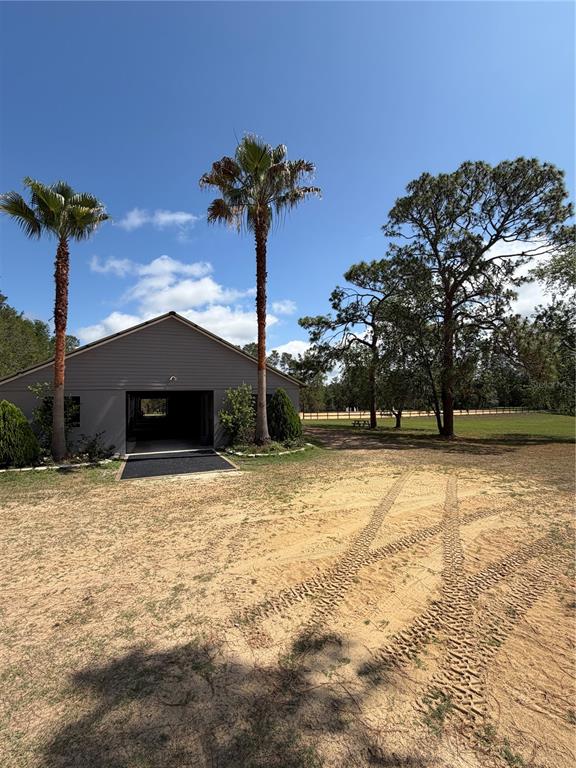 A gray barn stands on a sandy lot with two palm trees and large pines — 4251 NE 136TH AVENUE, WILLISTON, FL