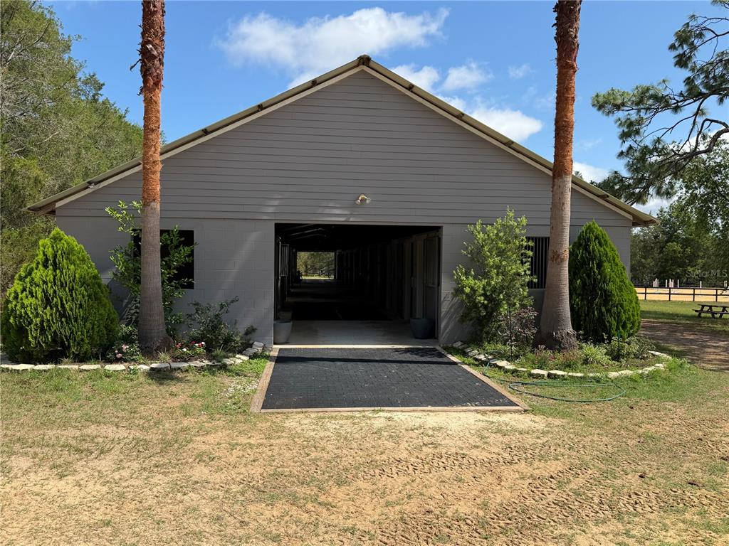 A gray barn with a center aisle, flanked by two palm trees and manicured shrubs — 4251 NE 136TH AVENUE, WILLISTON, FL