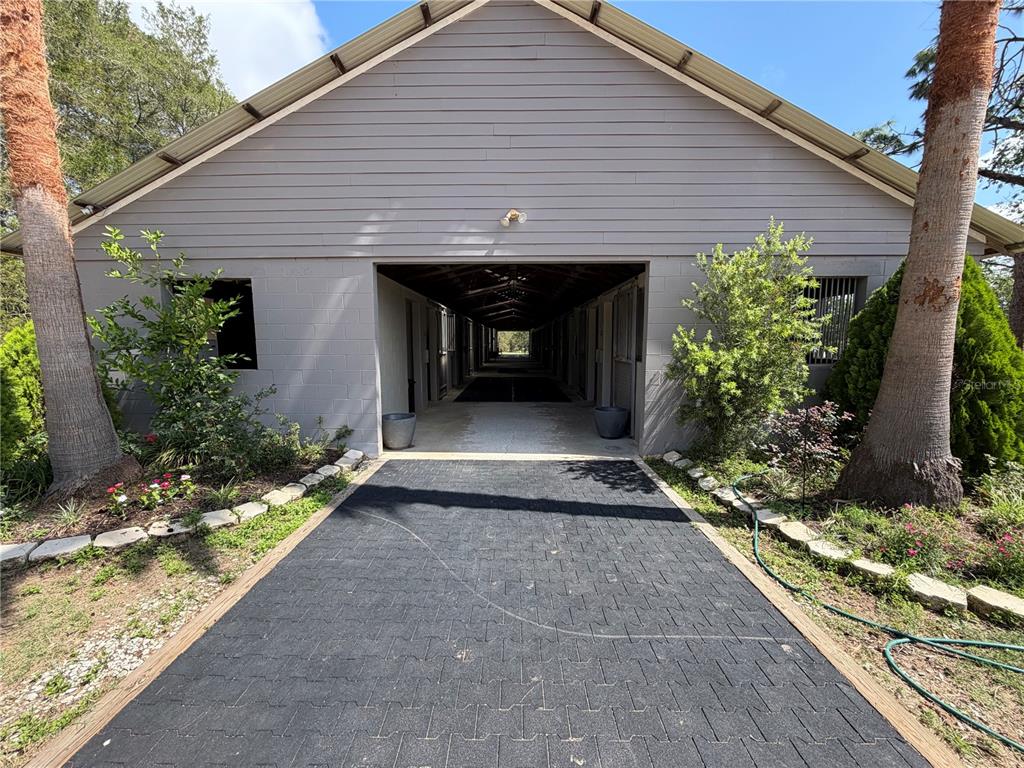 A gray barn with a central breezeway and a paved walkway leading to the entrance — 4251 NE 136TH AVENUE, WILLISTON, FL