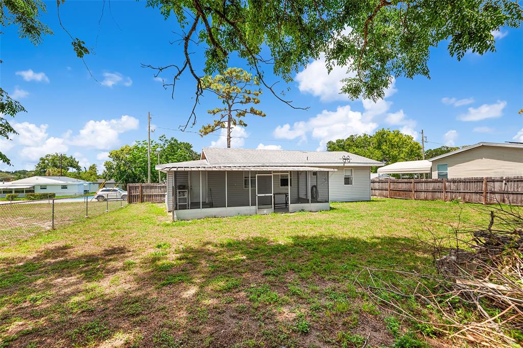 The exterior of a single-story house features a screened-in porch and a large backyard — 39014 KIRKLAND DRIVE, ZEPHYRHILLS, FL