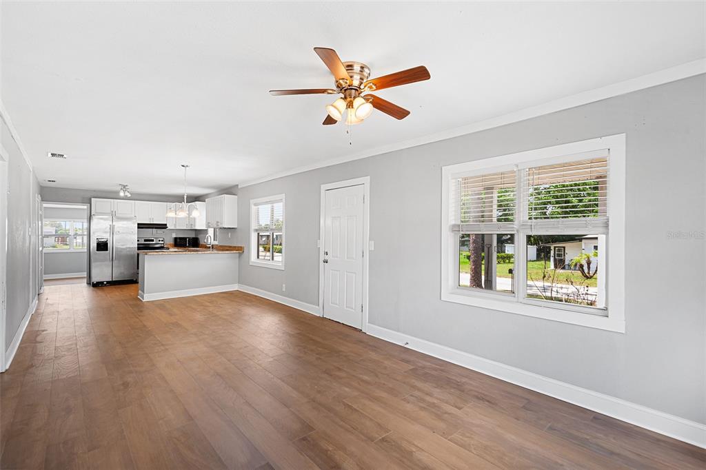 An open-concept living area with light gray walls, wood-look flooring, and an adjacent kitchen — 39014 KIRKLAND DRIVE, ZEPHYRHILLS, FL