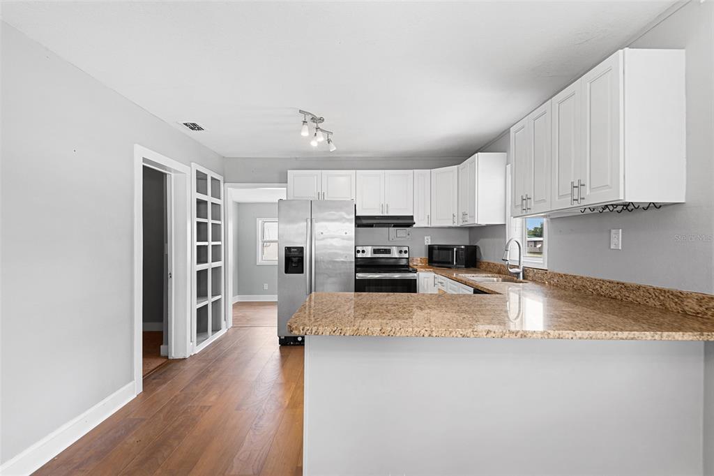A kitchen with white cabinets, granite countertops, stainless steel appliances, and wood-look flooring — 39014 KIRKLAND DRIVE, ZEPHYRHILLS, FL