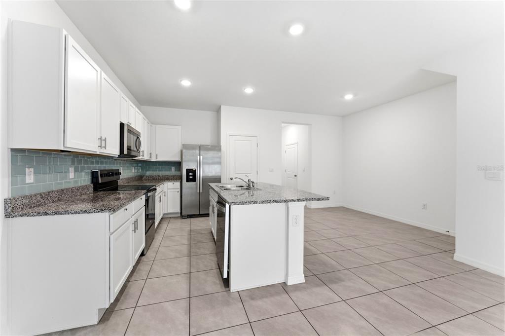 A kitchen features white cabinets, granite countertops, a center island, and light-colored tile flooring — 16632 GROTTO STEAM PLACE, WIMAUMA, FL