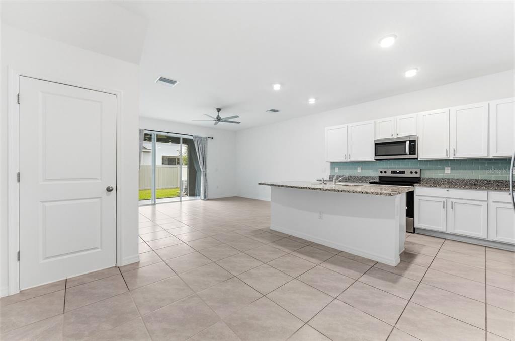 An open-concept kitchen with white cabinets, granite countertops, and tile flooring leads to a patio — 16632 GROTTO STEAM PLACE, WIMAUMA, FL
