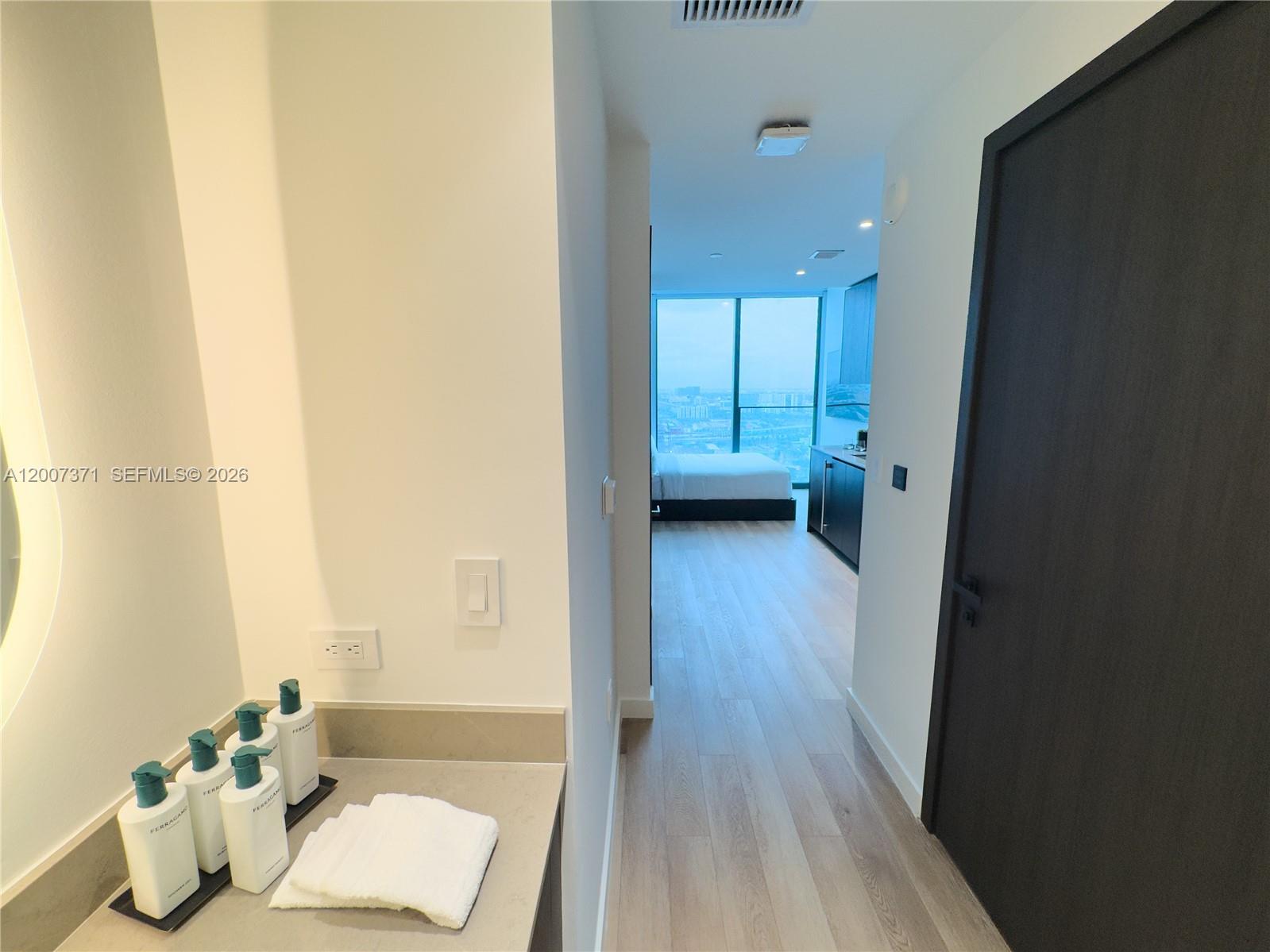 A bathroom vanity with toiletries leads into a bedroom with floor-to-ceiling windows — 20 NE 11th St # 3012B, Miami FL 33132, MIAMI, FL