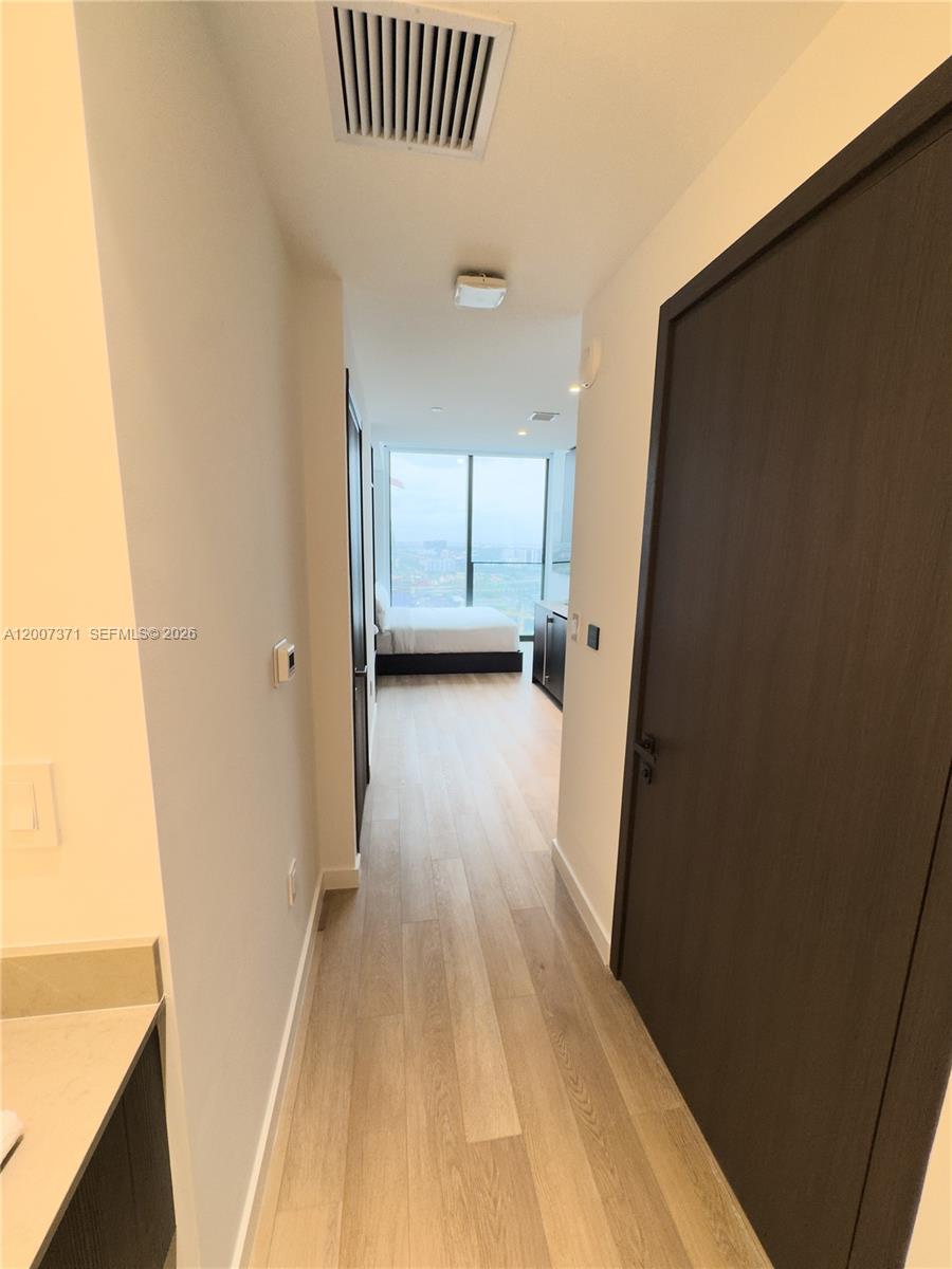 A hallway with light wood flooring leads to a bedroom with floor-to-ceiling windows — 20 NE 11th St # 3012B, Miami FL 33132, MIAMI, FL