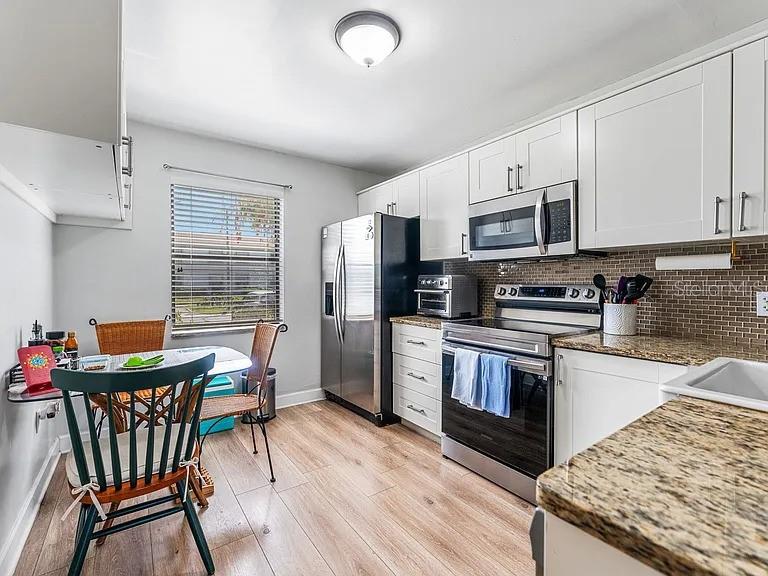 A kitchen features white cabinets, stainless steel appliances, granite countertops, and a small dining area — 109 MEADOW LANE, OLDSMAR, FL