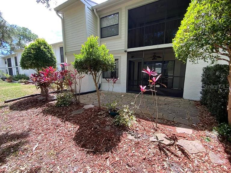 A backyard patio features a screened-in porch, stone pavers, and various shrubs and plants — 109 MEADOW LANE, OLDSMAR, FL