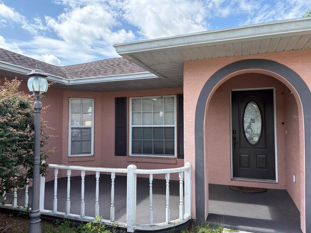 A pink stucco house exterior features a front porch with a white railing and arched entryway — 126 BRIGHTON CIRCLE, AUBURNDALE, FL