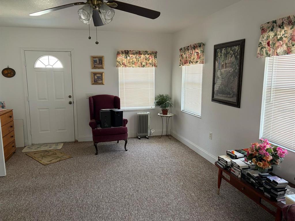 A living room features a burgundy armchair, a ceiling fan, and windows with floral valances — 126 BRIGHTON CIRCLE, AUBURNDALE, FL