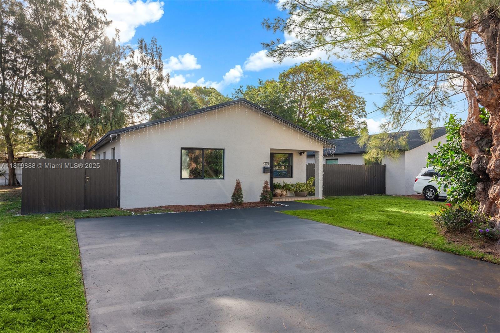 A single-story house with a light-colored stucco exterior, a dark roof, and a paved driveway — 311 SE 3rd Ave, Hallandale Beach FL 33009, HALLANDALE BEACH, FL