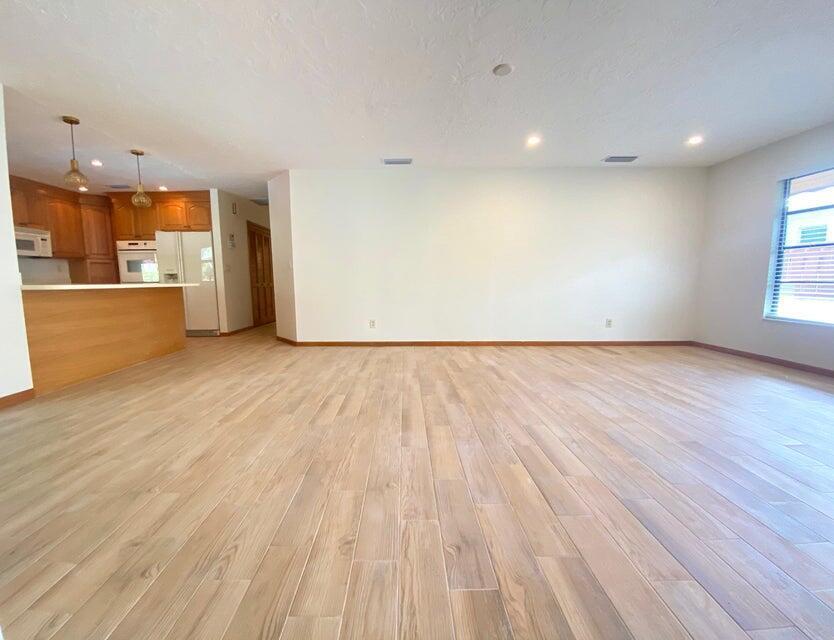 A spacious room with light wood-look tile flooring, white walls, and an open kitchen area — 5585 Pennock Point Road, Jupiter FL 33458, JUPITER, FL