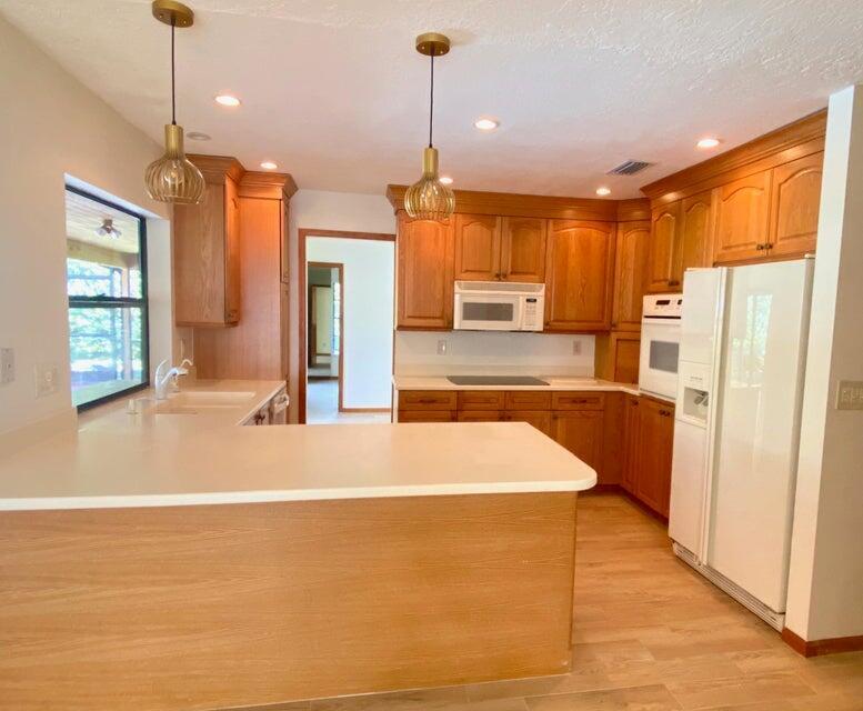 A kitchen with wood cabinets, white countertops, two pendant lights, and a white refrigerator — 5585 Pennock Point Road, Jupiter FL 33458, JUPITER, FL