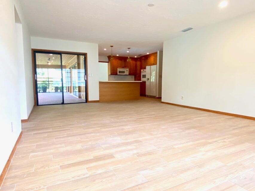 A living area with light wood-look tile flooring leads to an open kitchen and patio — 5585 Pennock Point Road, Jupiter FL 33458, JUPITER, FL