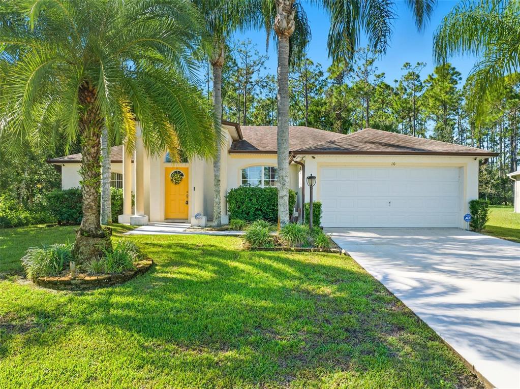 A single-story house with a yellow front door, a two-car garage, and palm trees — 20 SEAMAN TRAIL N, PALM COAST, FL