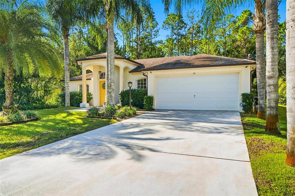 A single-story house with a white garage, yellow front door, and palm trees in front — 20 SEAMAN TRAIL N, PALM COAST, FL