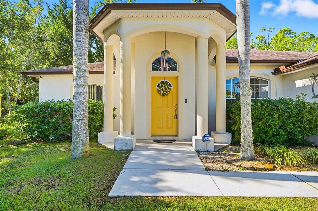 A yellow front door with a wreath sits under a covered entryway with white columns — 20 SEAMAN TRAIL N, PALM COAST, FL