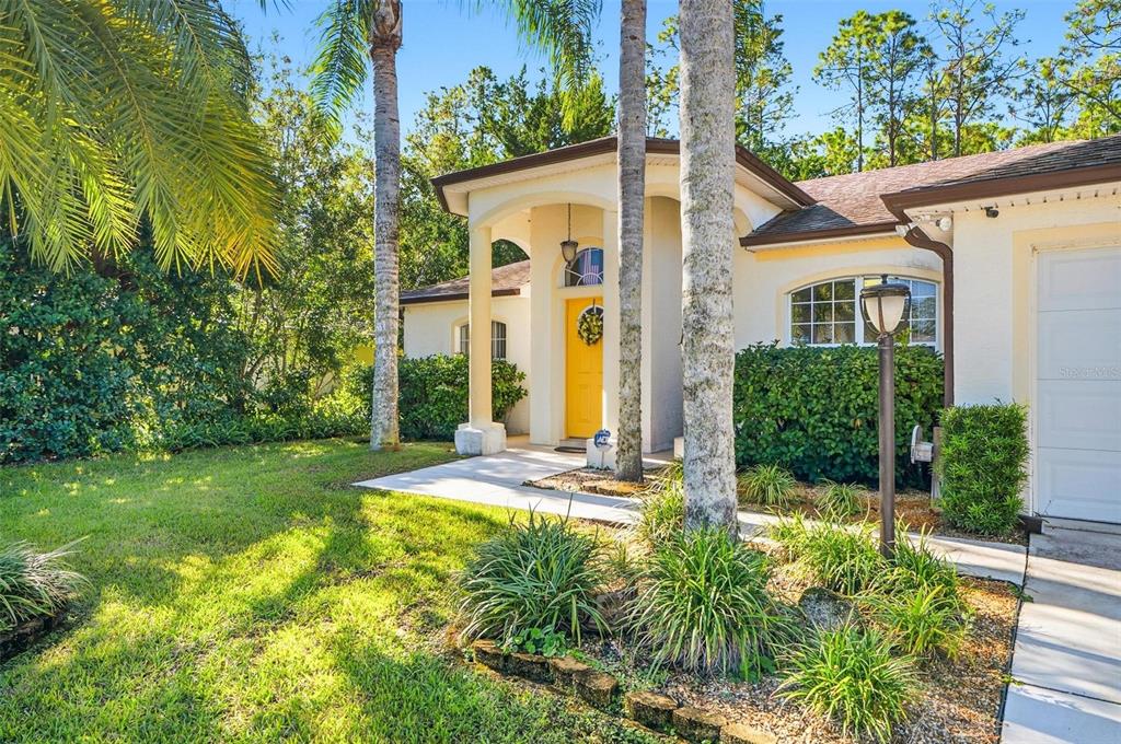 A single-story house with a yellow front door, arched entryway, and palm trees in front — 20 SEAMAN TRAIL N, PALM COAST, FL