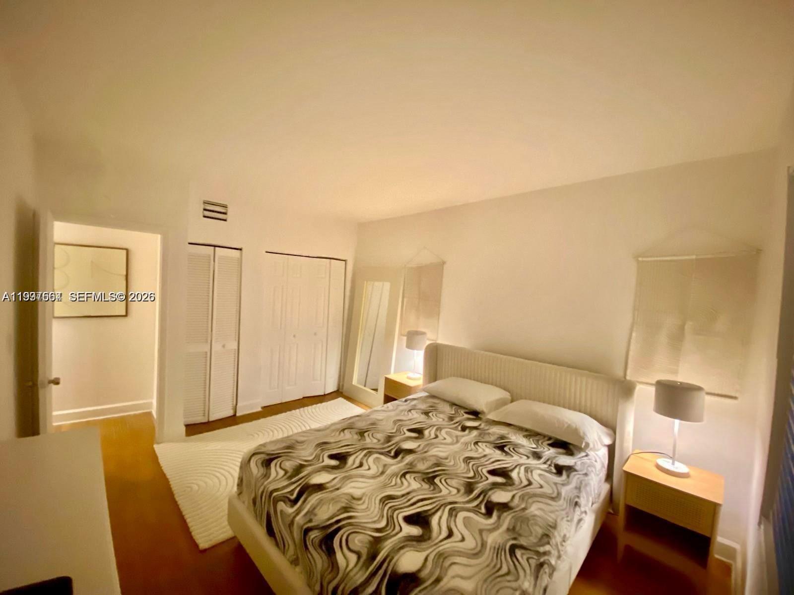 A bedroom features a bed with a patterned comforter, two nightstands, and white closet doors — 605 Euclid Ave # 103, Miami Beach FL 33139, MIAMI BEACH, FL