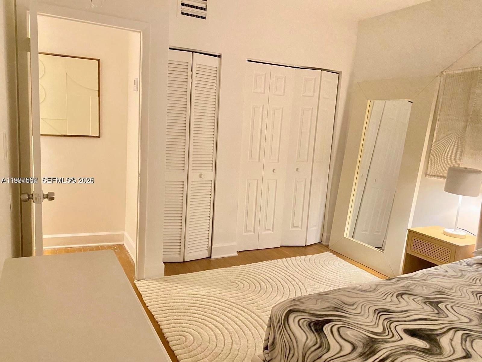 A bedroom features a white rug, two sets of closet doors, and a floor mirror — 605 Euclid Ave # 103, Miami Beach FL 33139, MIAMI BEACH, FL