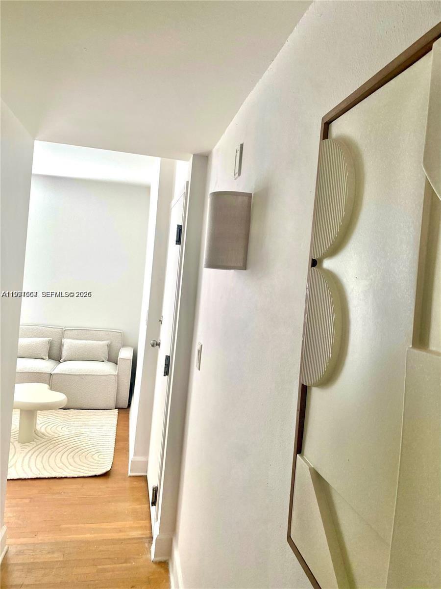 A hallway with a wall-mounted light fixture leads to a room with a sofa — 605 Euclid Ave # 103, Miami Beach FL 33139, MIAMI BEACH, FL