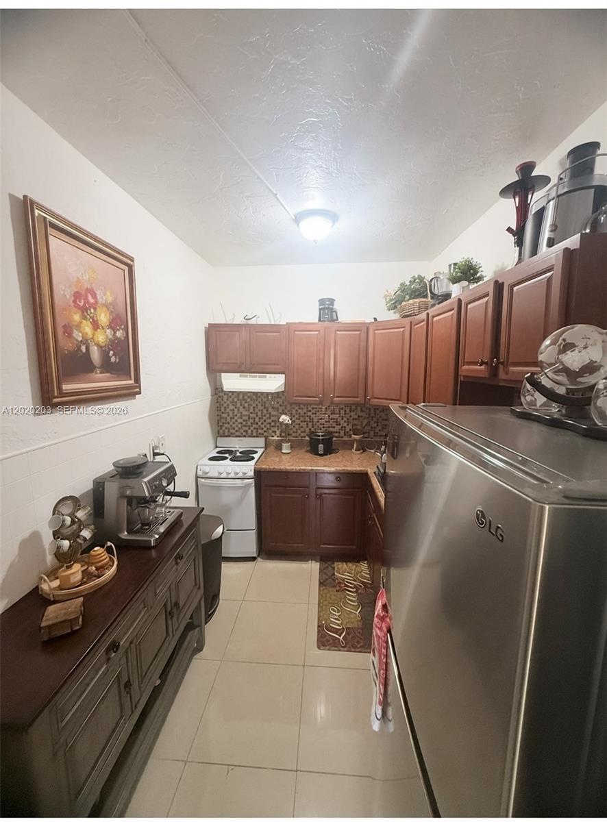 A narrow kitchen features brown cabinets, stainless steel appliances, and a wooden sideboard — 12680 NE 3rd Ave # B, North Miami FL 33161, NORTH MIAMI, FL