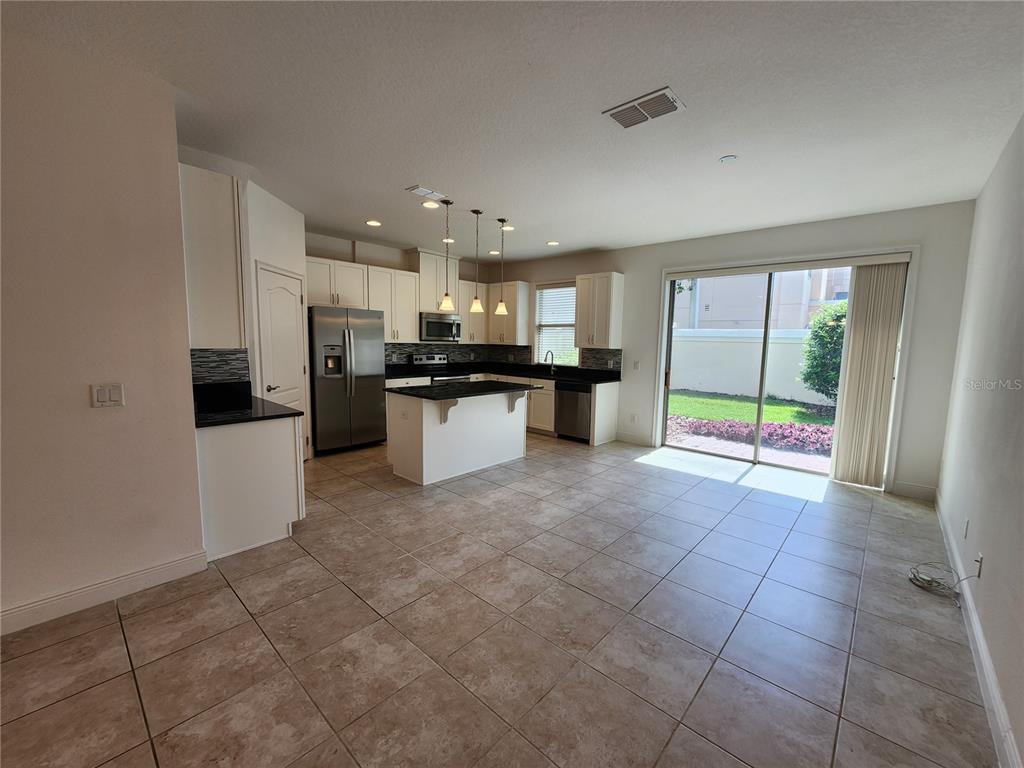 A kitchen with white cabinets, dark countertops, and tile flooring opens to a backyard patio — 9805 WINNINGTON STREET, ORLANDO, FL