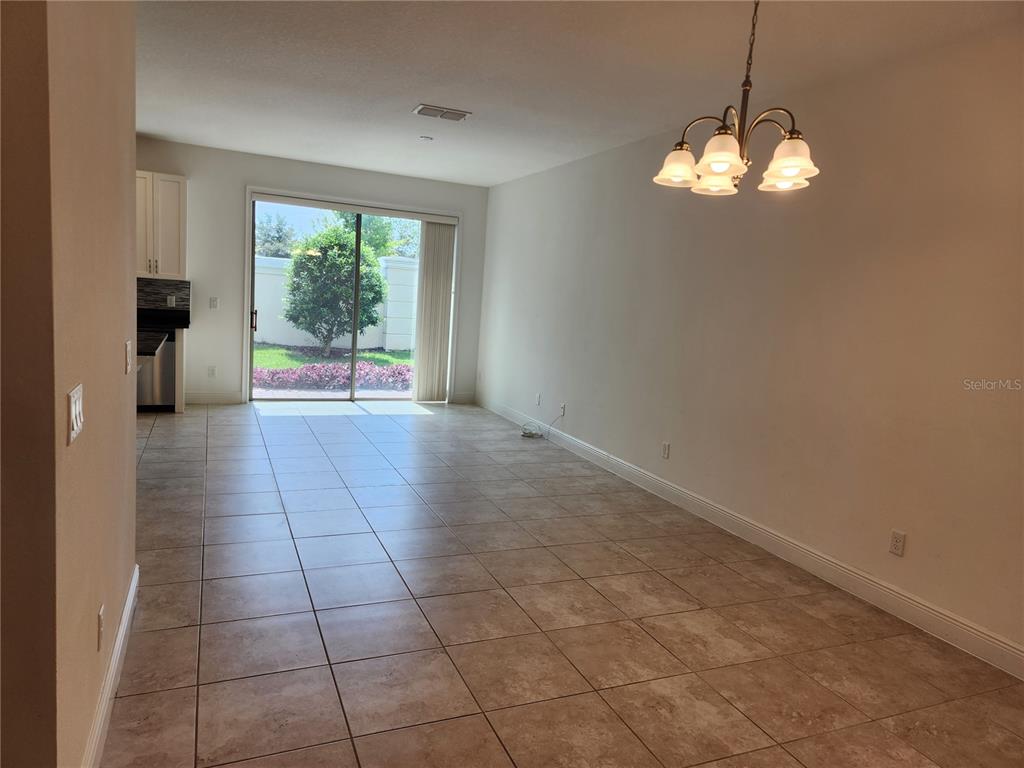 An open-concept living and dining area features tile flooring, a chandelier, and sliding glass doors — 9805 WINNINGTON STREET, ORLANDO, FL