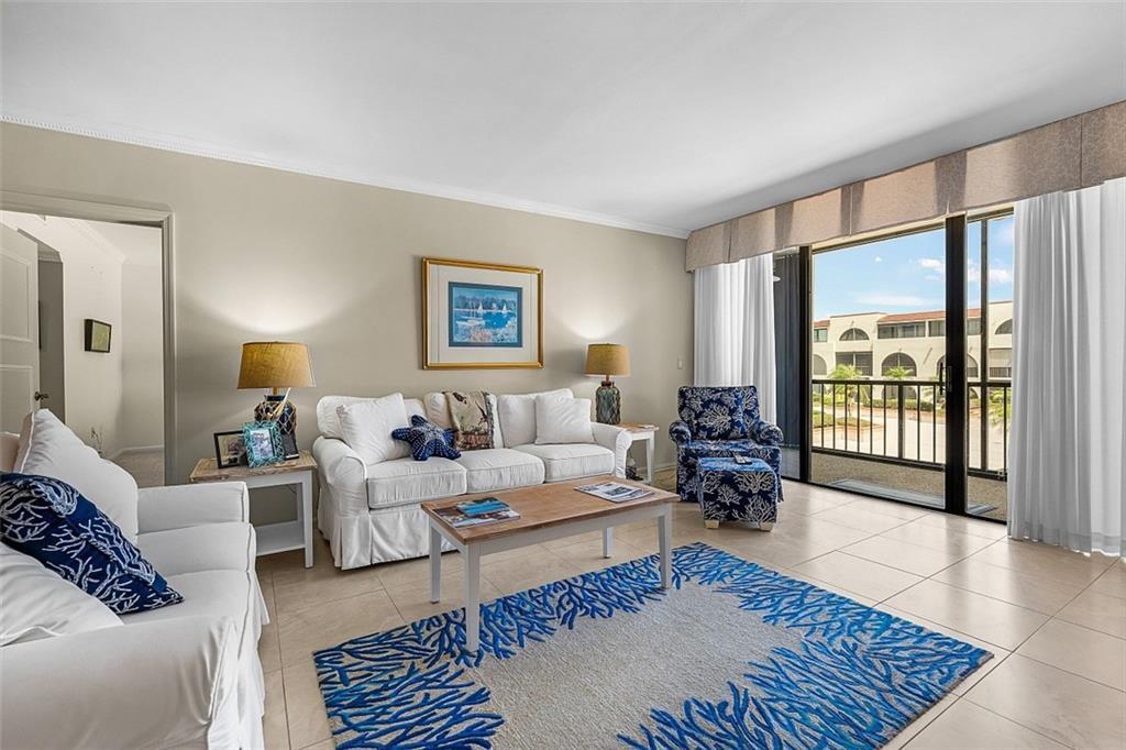 A living room features white sofas, a patterned area rug, and a sliding glass door — VERO BEACH, FL