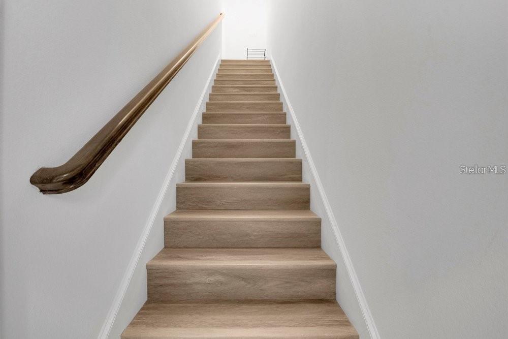 A straight staircase with light wood-look steps and a wooden handrail against white walls — 15026 SUMMER HARVEST STREET, WINTER GARDEN, FL