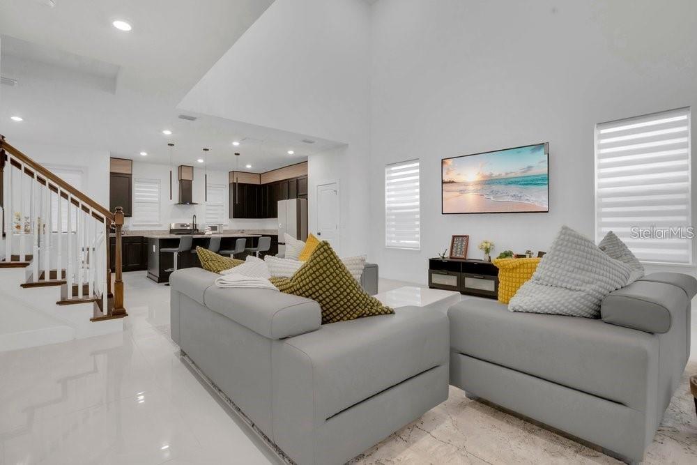 A bright living room with gray sofas, a high ceiling, and an open-concept kitchen — 15026 SUMMER HARVEST STREET, WINTER GARDEN, FL