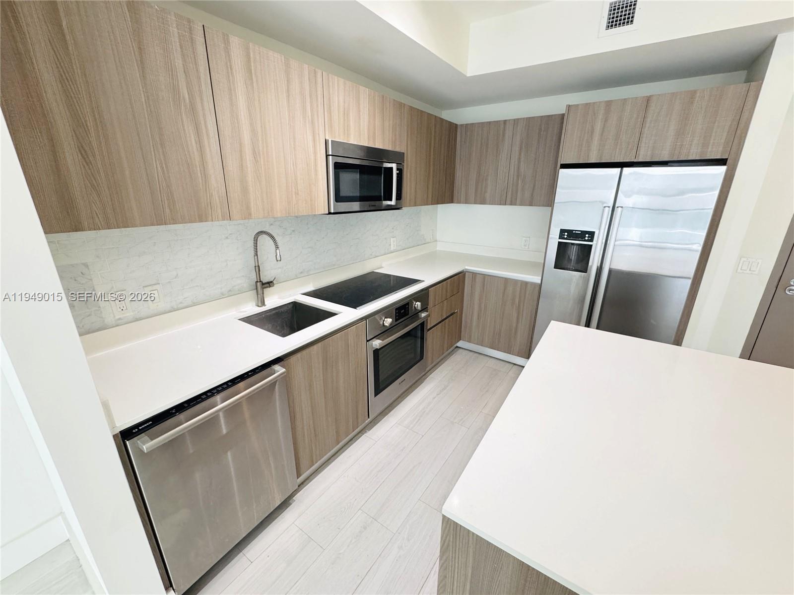 A modern kitchen features light wood cabinets, stainless steel appliances, and white quartz countertops — 201 SW 17th Rd # 603, Miami FL 33129, MIAMI, FL