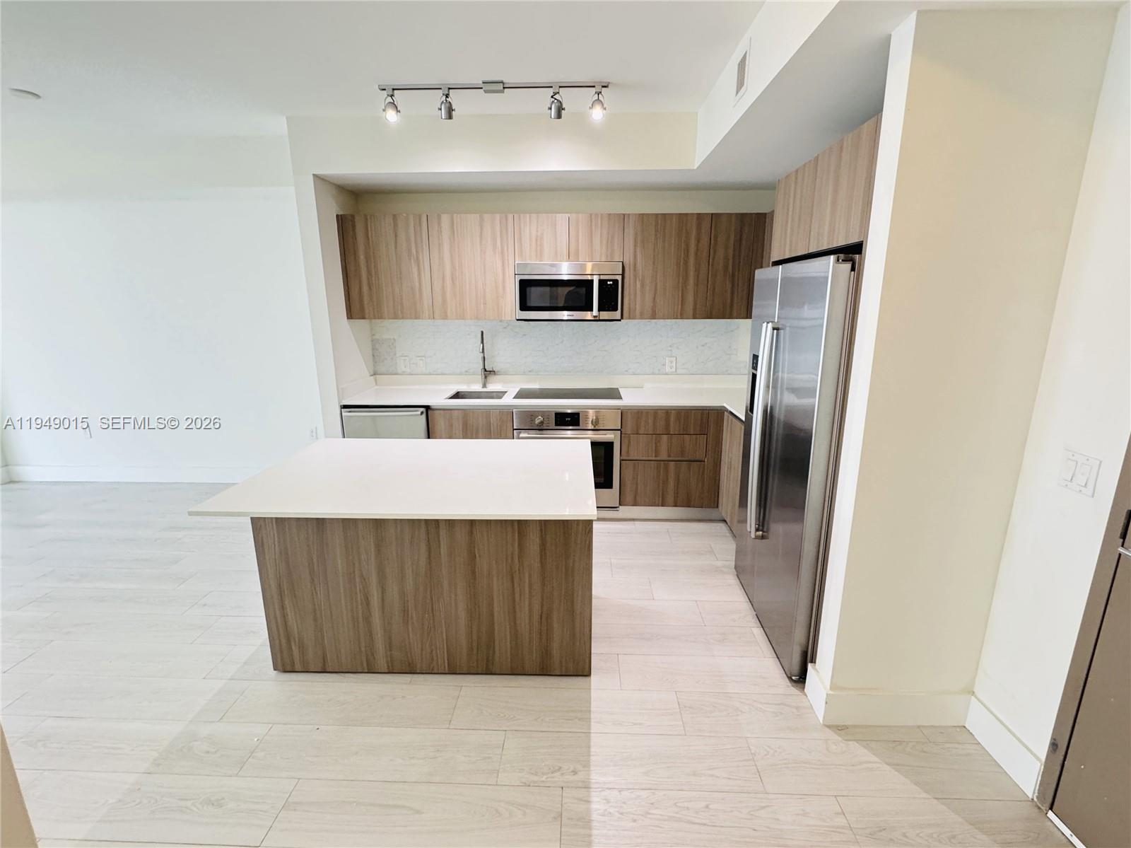 A modern kitchen features wood-grain cabinets, stainless steel appliances, and a white island countertop — 201 SW 17th Rd # 603, Miami FL 33129, MIAMI, FL