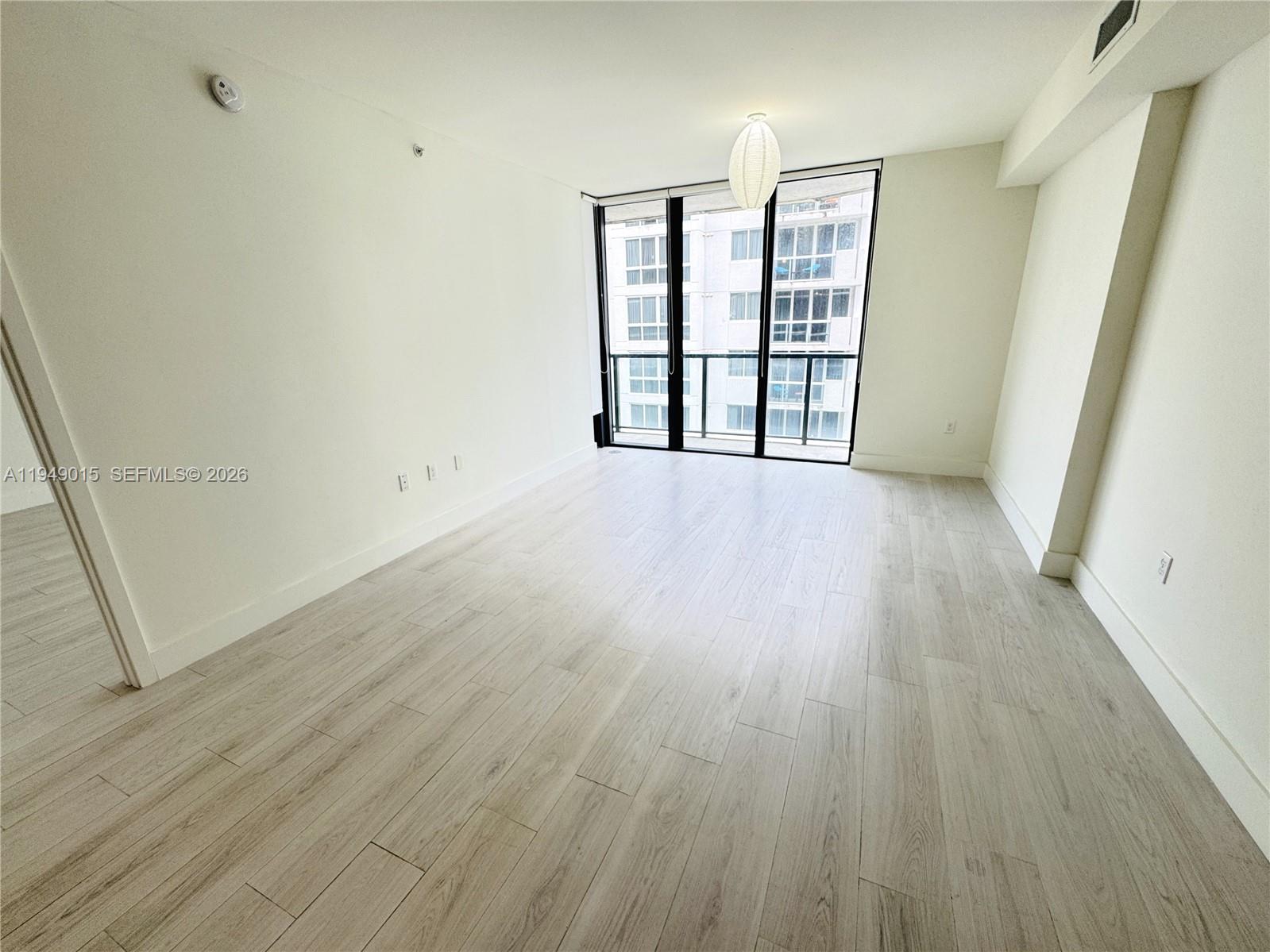 An empty room features light wood-look flooring, white walls, and a large glass balcony door — 201 SW 17th Rd # 603, Miami FL 33129, MIAMI, FL
