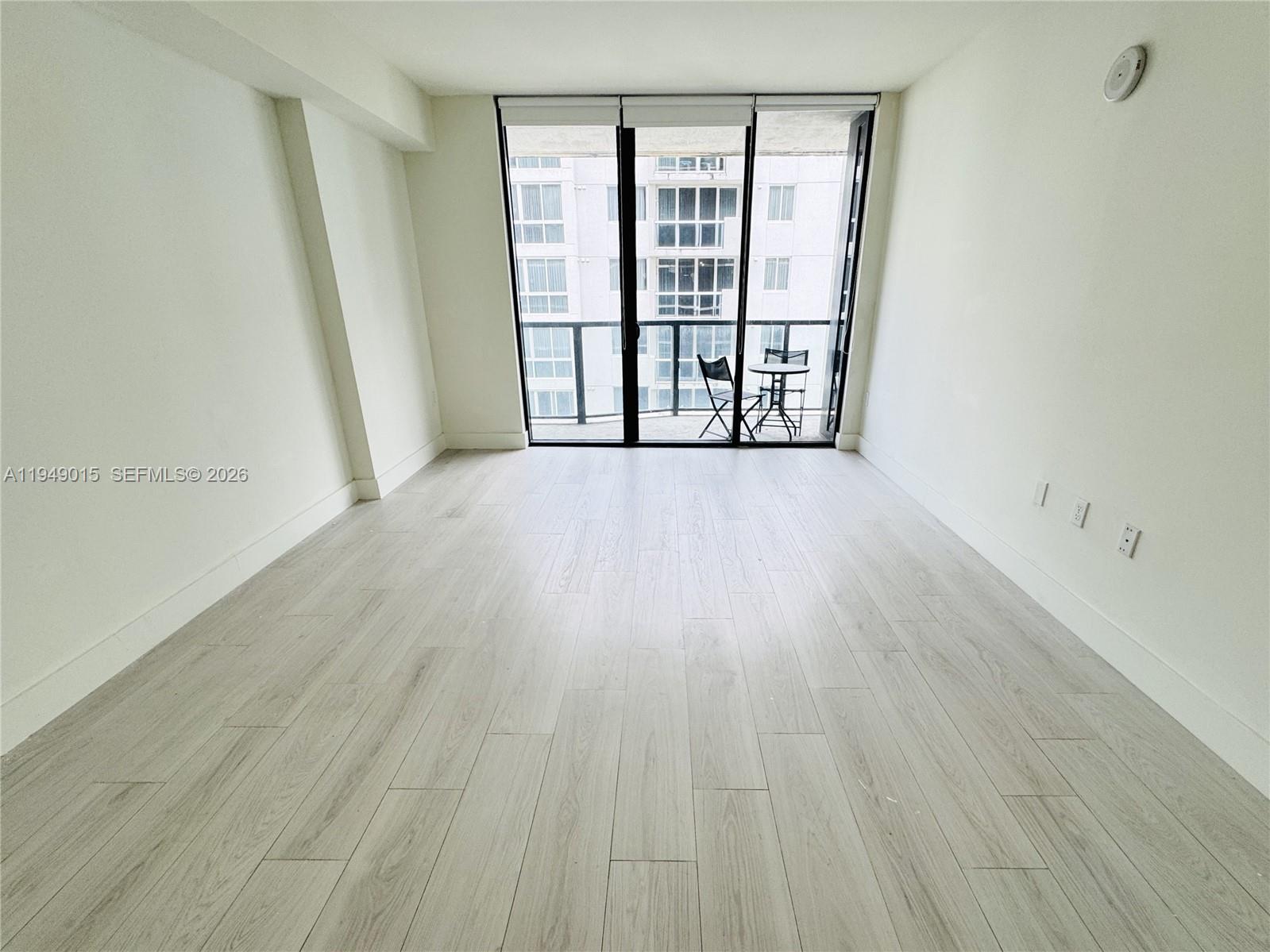 An empty room features light wood-look flooring, white walls, and a balcony with outdoor furniture — 201 SW 17th Rd # 603, Miami FL 33129, MIAMI, FL