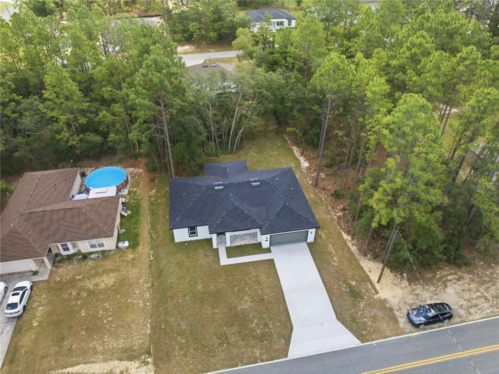 An aerial view shows a single-story house with a dark roof, driveway, and surrounding trees — 7605 N SANTOS DRIVE, CITRUS SPRINGS, FL