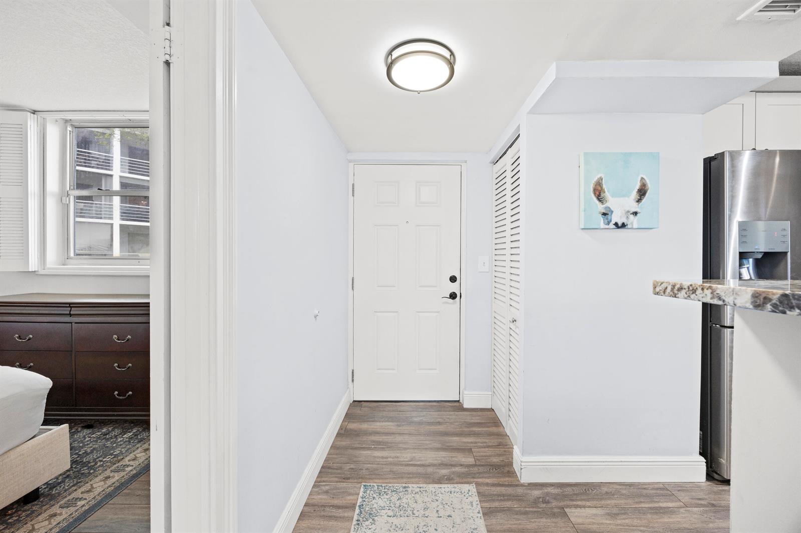 An entryway features wood-look flooring, a white door, a louvered closet, and a llama painting — 5301 NW 2nd Avenue # 1010, Boca Raton FL 33487, BOCA RATON, FL