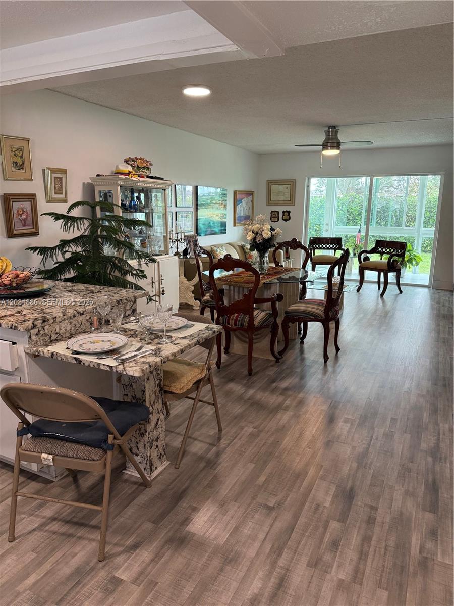 An open-concept dining and kitchen area features granite countertops, wood-look flooring, and a glass-topped table — 600 NW 77th Ave # 108, Margate FL 33063, MARGATE, FL
