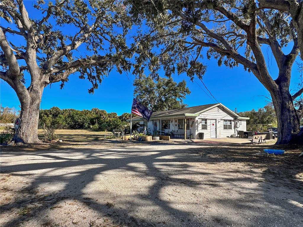 A single-story house with a gravel driveway sits between two large, moss-draped oak trees — 2519 MOCCASIN WALLOW ROAD, PALMETTO, FL