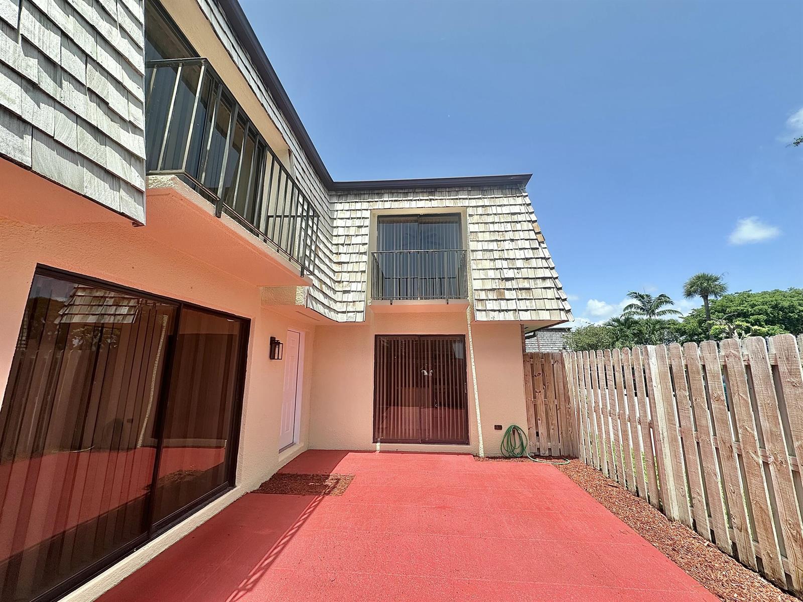 A two-story building exterior features a red patio, wooden fence, and upper-level balconies — 255 Lake Arbor Drive, Palm Springs FL 33461, PALM SPRINGS, FL